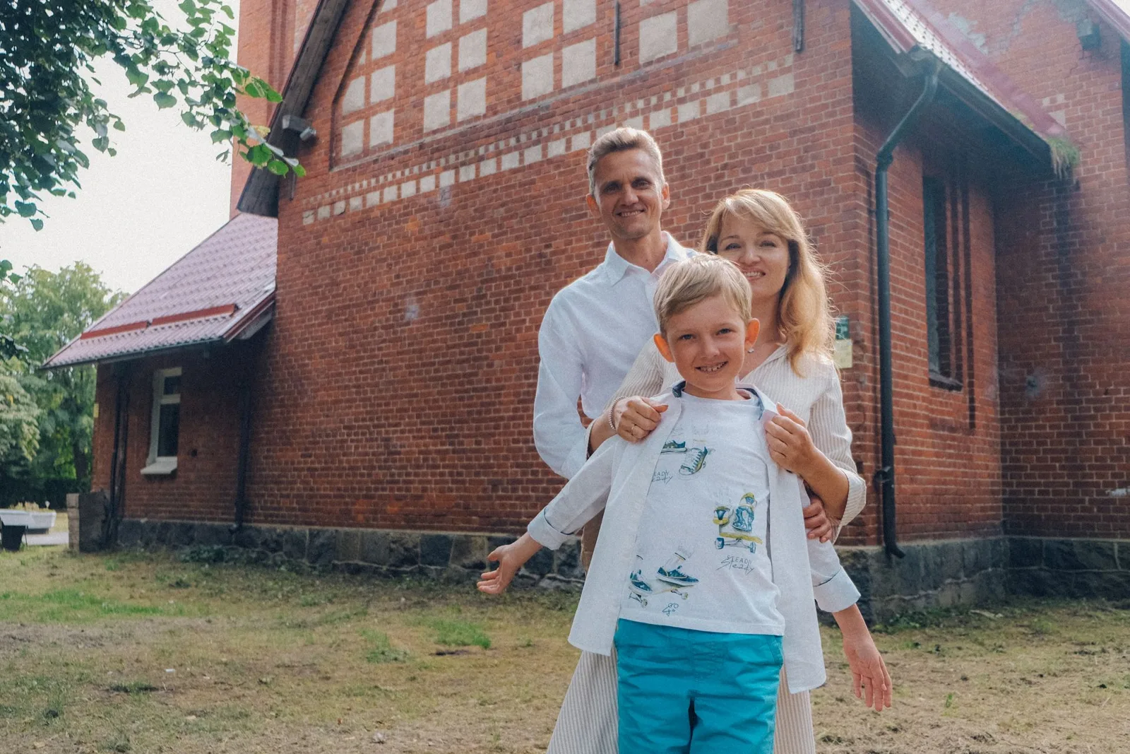 Семья у стены из красного кирпича: мальчик в белой футболке впереди, родители за его спиной. Фото: Настя Шафранова
