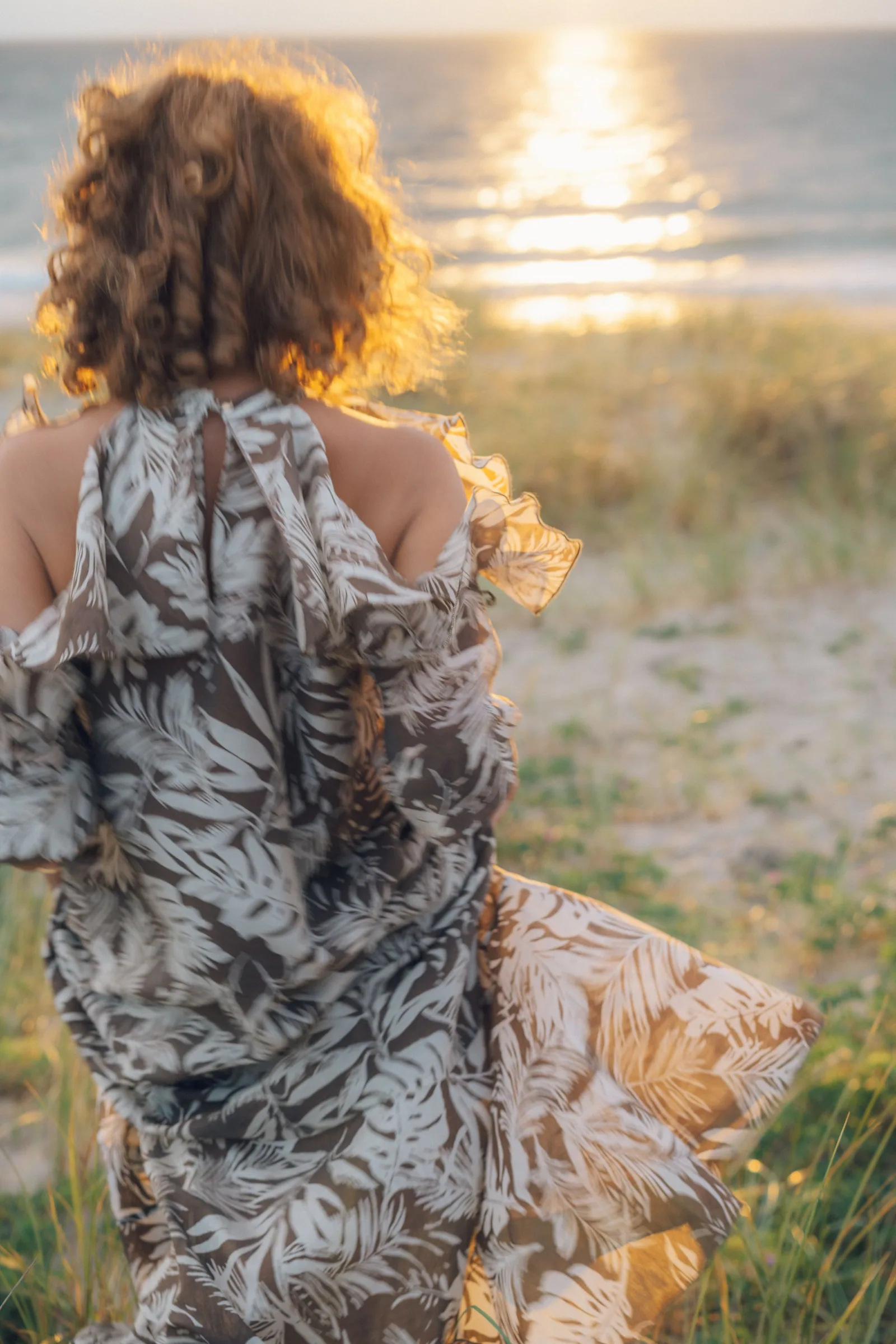 Спиной к нам, кудри горят против солнца. Платье с листьями надувается на ветру, впереди солнечная дорожка