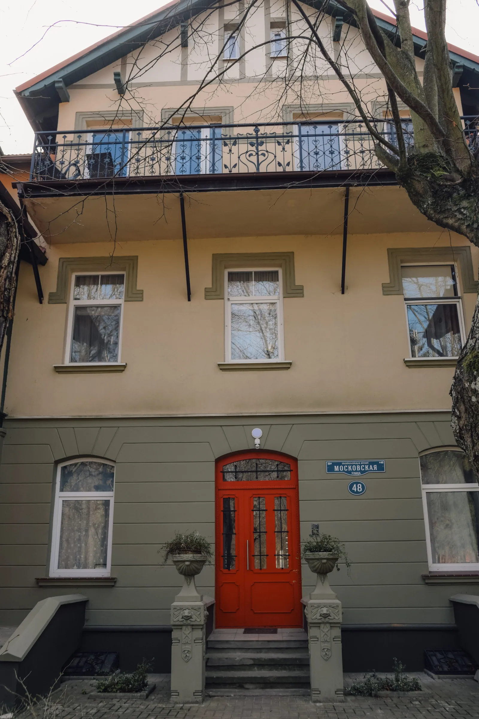 Красная дверь под полукруглым окном, две вазы на столбиках у ступеней, над входом балкон